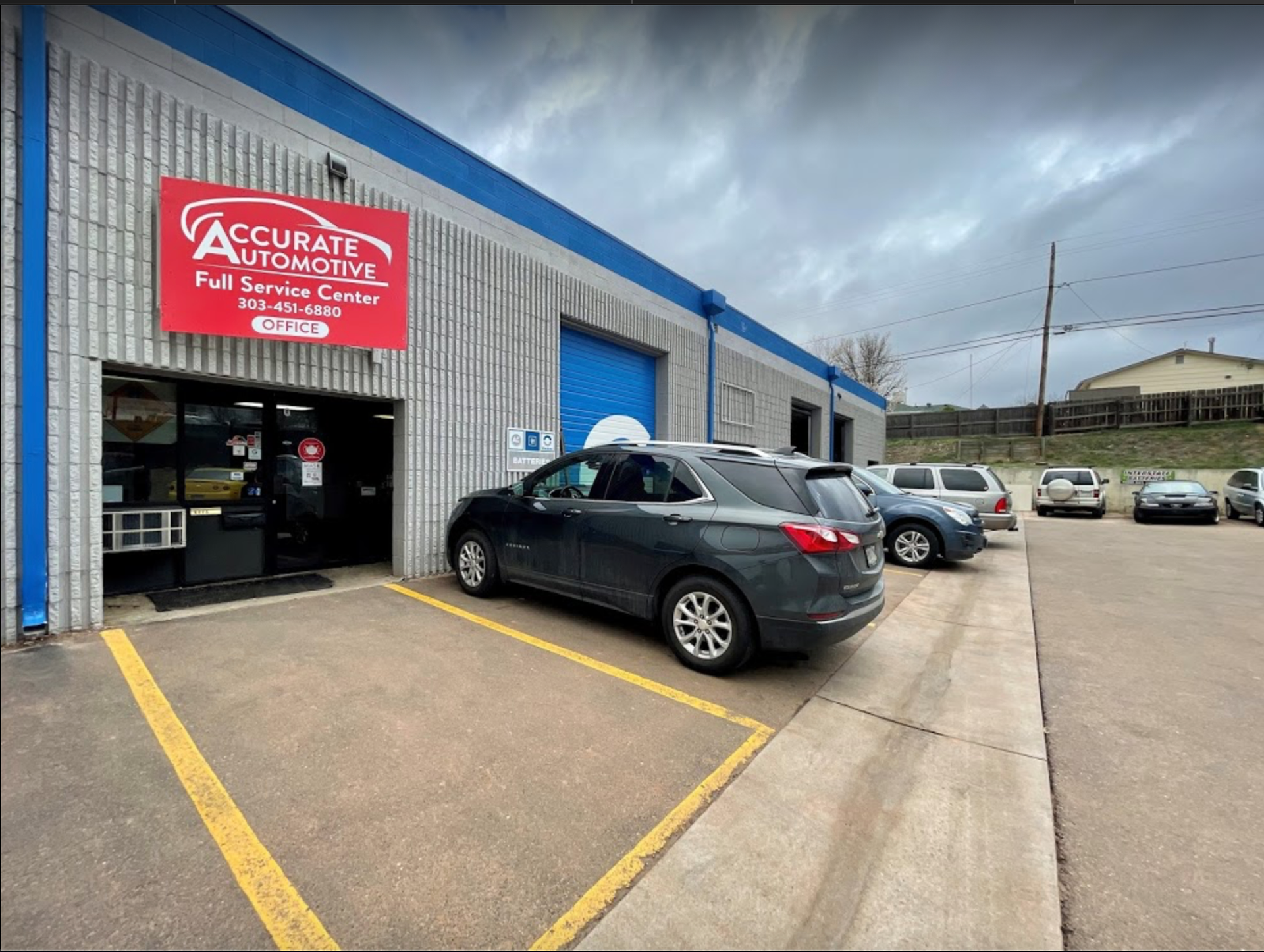 Auto repair shop with blue siding, open garage bay, and cars parked outside under cloudy sky | Accurate Automotive Northglenn