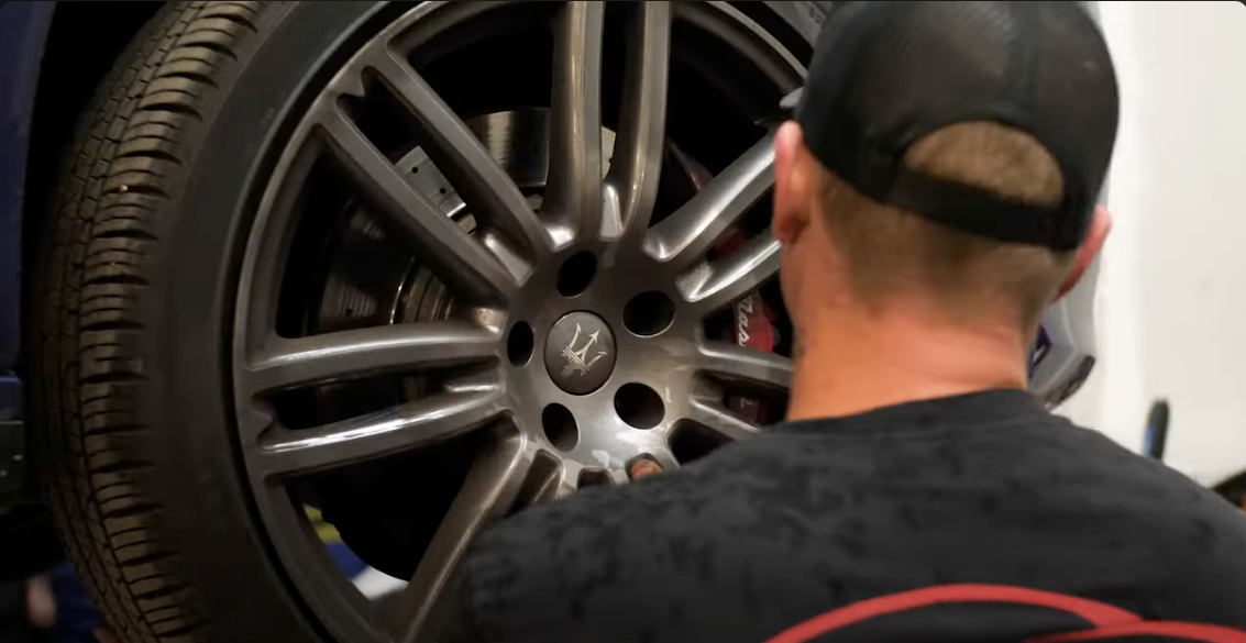Person in a black cap inspecting a dark alloy car wheel in a garage | Accurate Automotive Northglenn