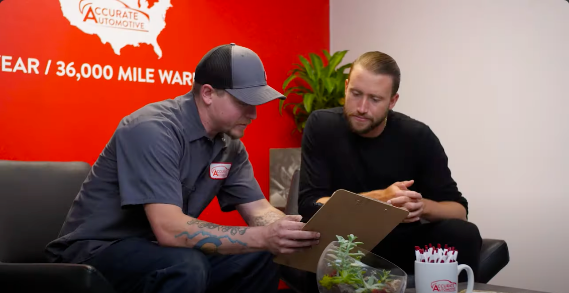 Two men sit on a couch reviewing paperwork in a red office lounge. | Accurate Automotive Northglenn