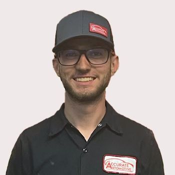 Smiling man in glasses and a black cap and shirt with a red logo, standing against a light background | Accurate Automotive