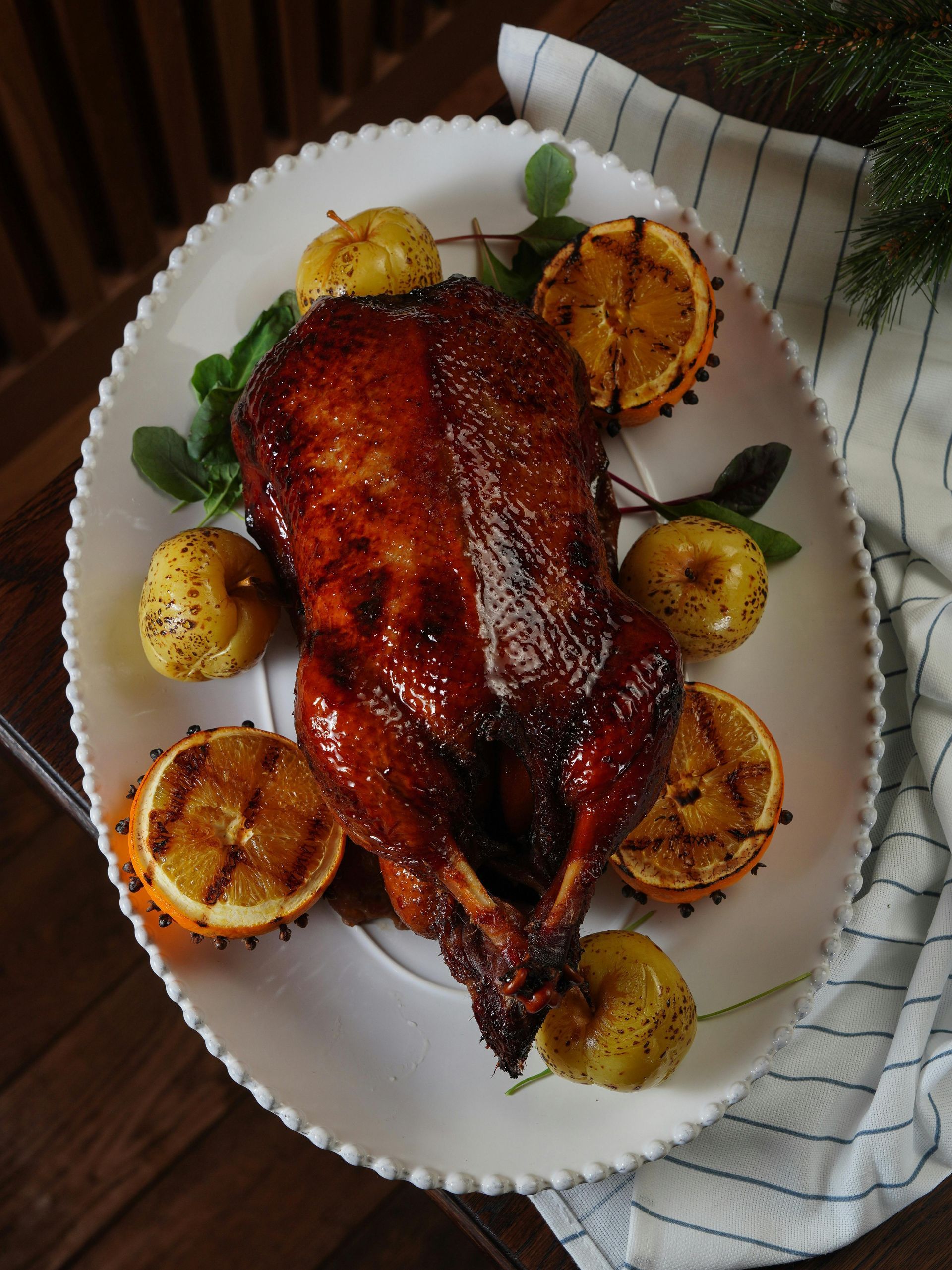 Roasted duck on a white platter with citrus and apples, wooden background.