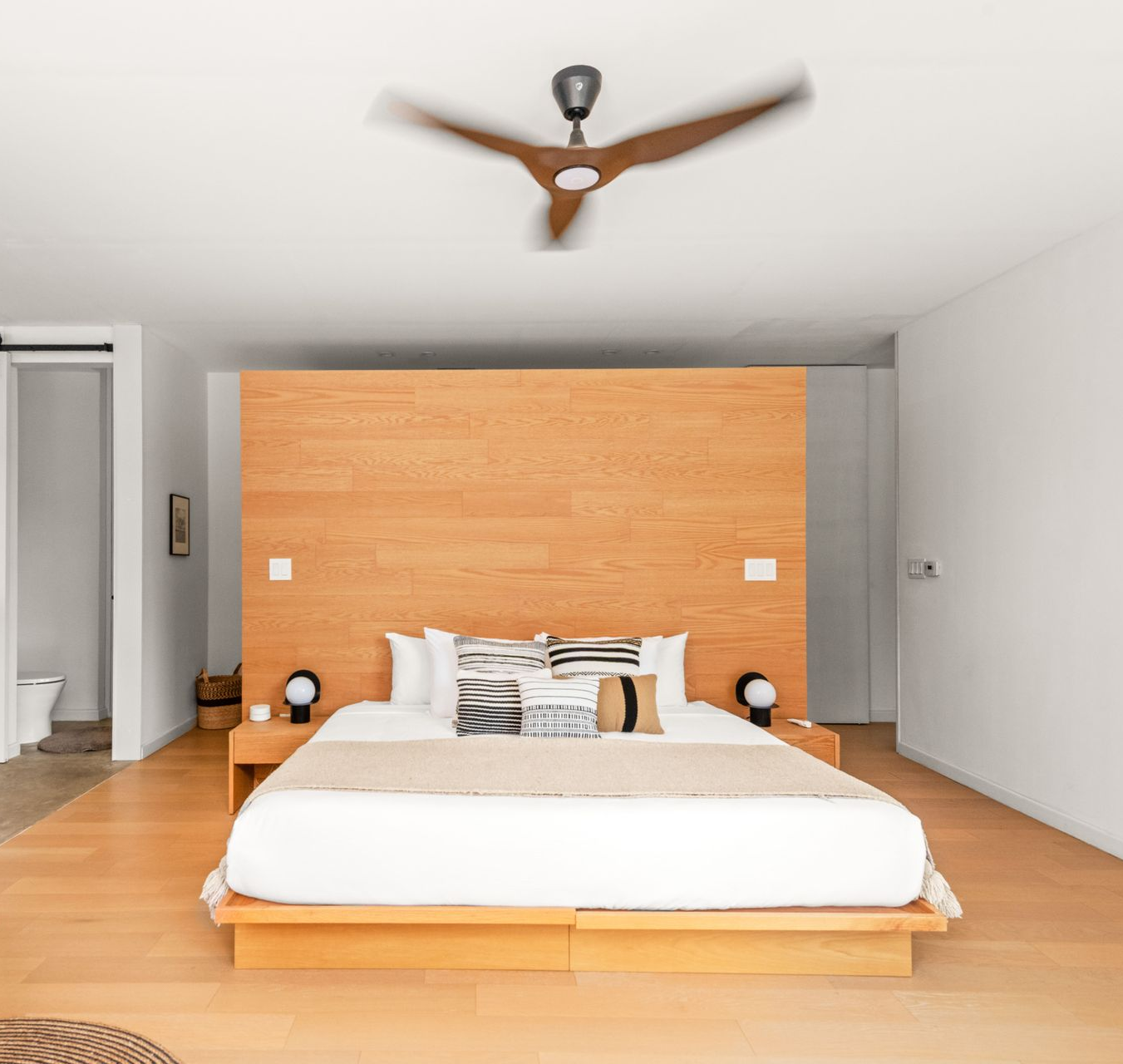 Dormitorio moderno con cama de madera, cabecero grande, ropa de cama blanca y ventilador de techo.