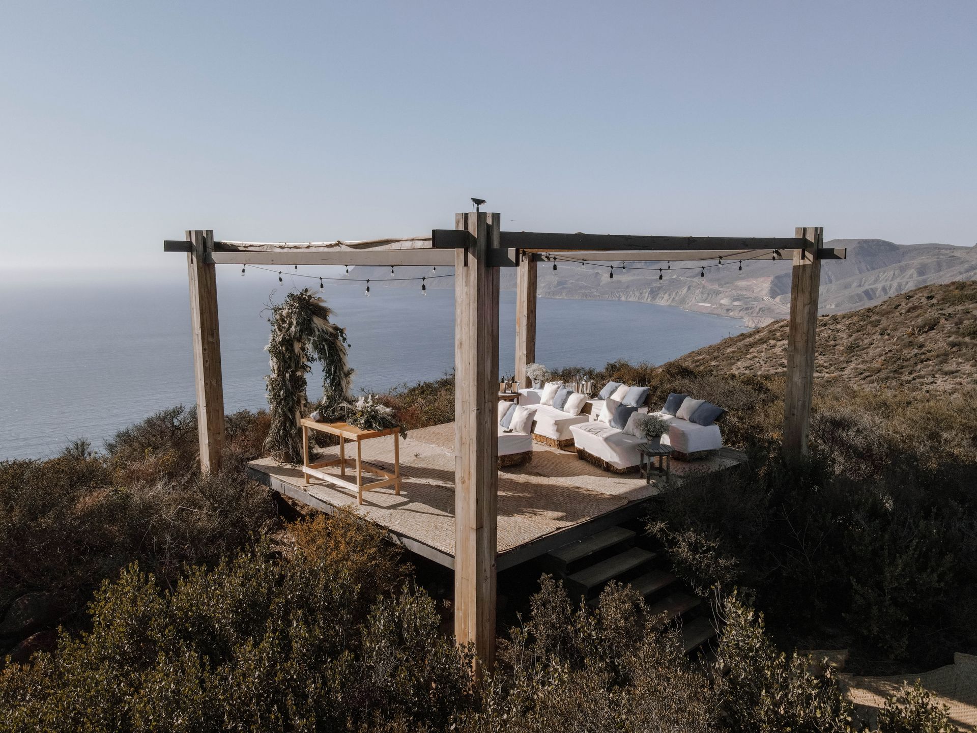 Terraza de madera frente al mar con tumbonas blancas bajo una pérgola con vistas al mar.