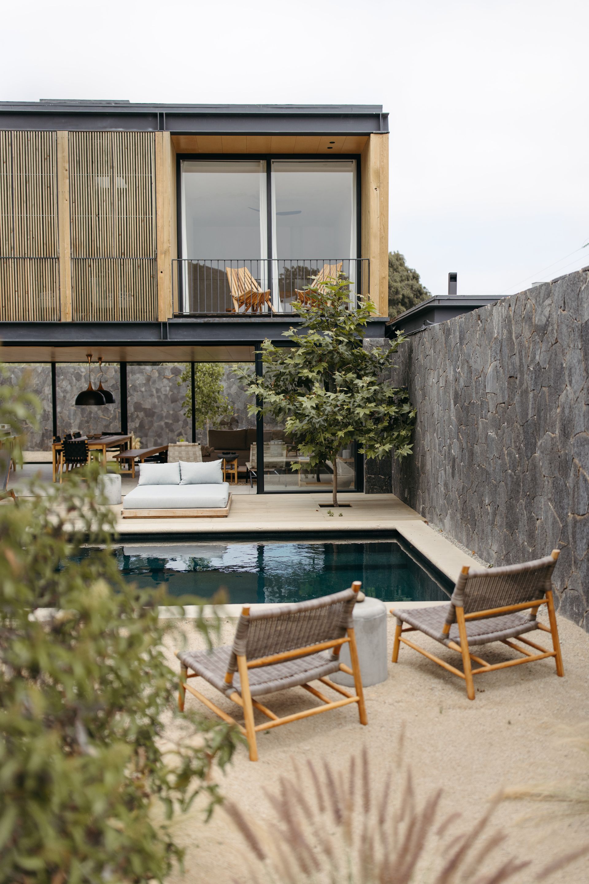 Patio moderno con piscina, tumbonas y una casa contemporánea con grandes ventanales y vegetación.