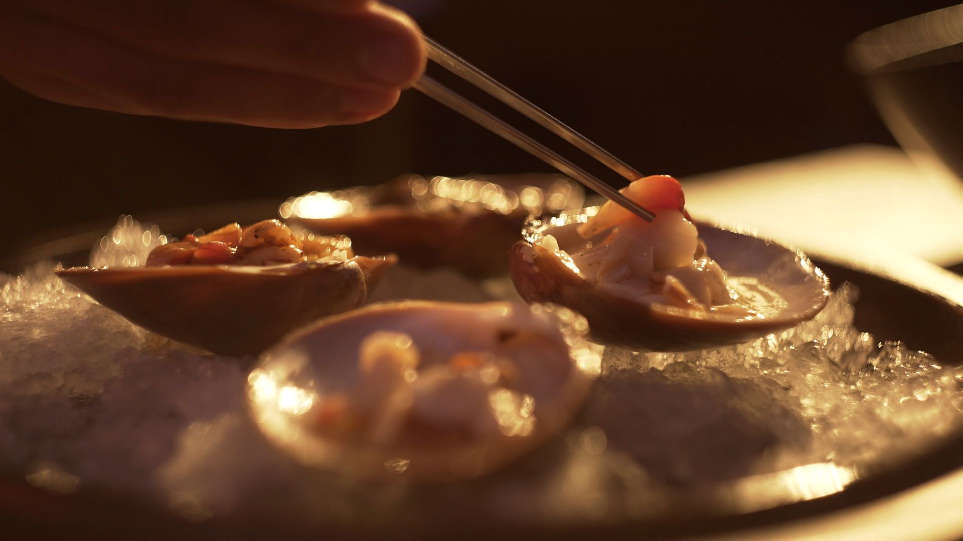 Una mano coloca un bocado de comida en una cuchara con aperitivos emplatados en una luz cálida y tenue.