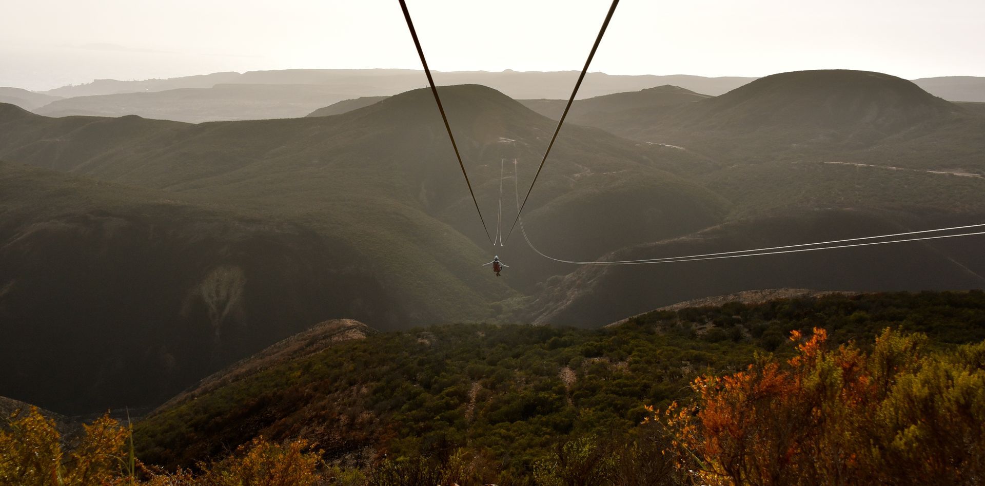Un parapente sobrevuela un valle de montaña brumoso con colinas boscosas y follaje otoñal.