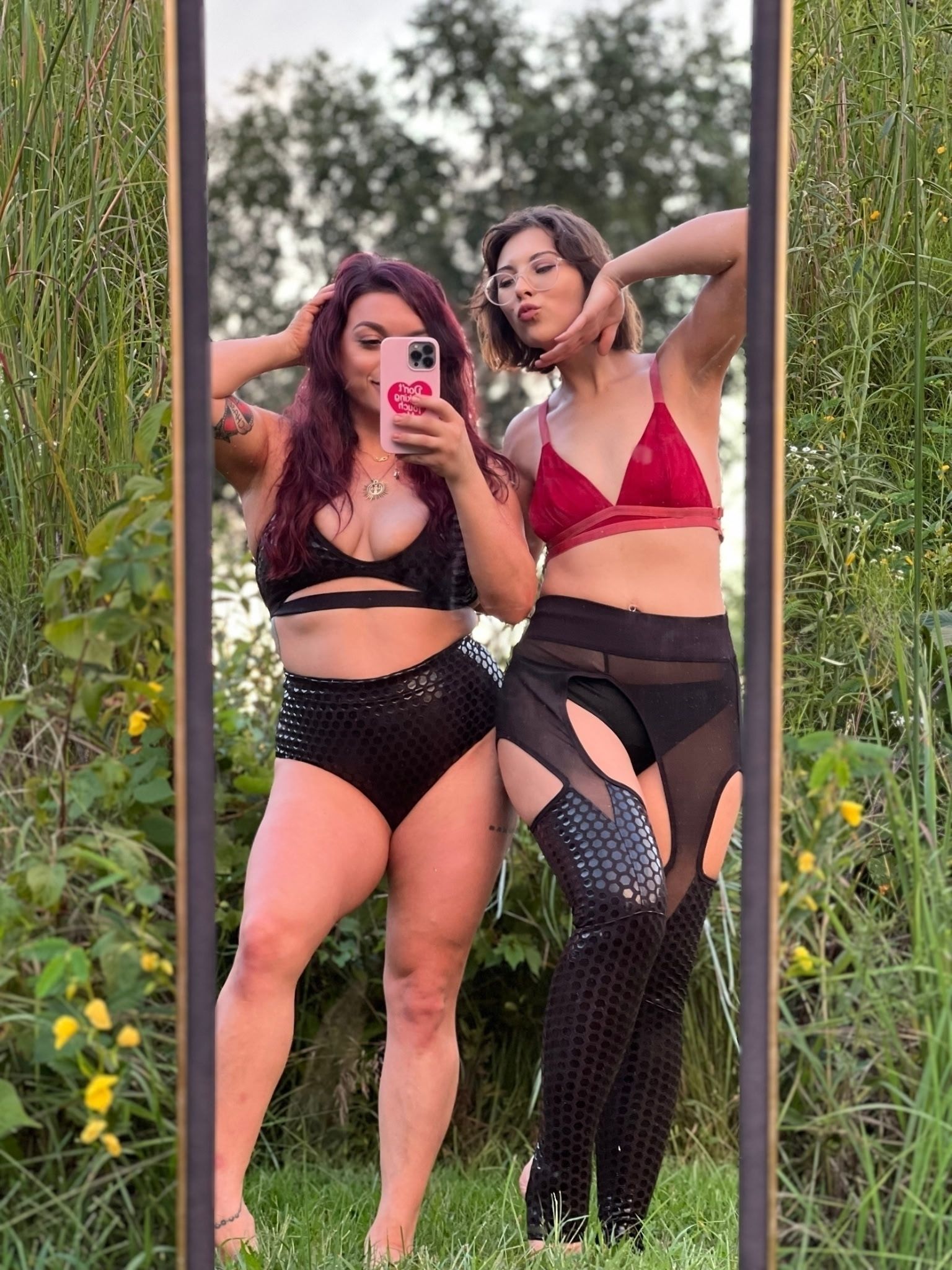 Two people posing for a mirror selfie outdoors in colorful pole-wear and sheer black cover-ups. Sticky Grippy Pole-wear