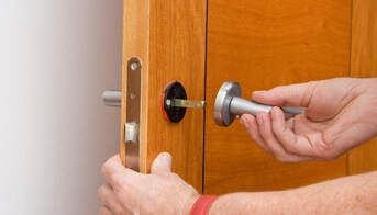 Picture of a handyman installing a new privacy set on a brown exterior door.