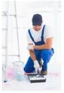Picture of a professional painter wearing white coveralls and holding a long painting rolling brush and bucket of paint.