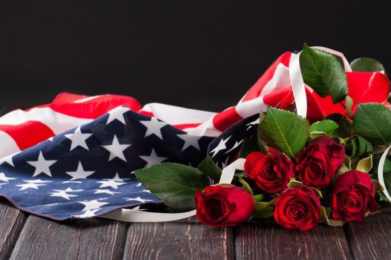 American flag draped beside red roses on a rustic wooden surface