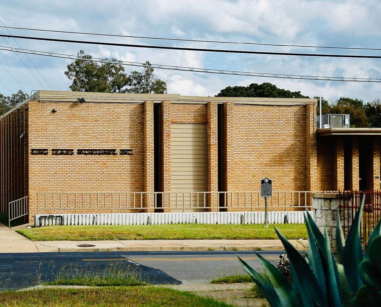 Modern wooden building with vertical slats, a low fence, and plants in front under a partly cloudy sky