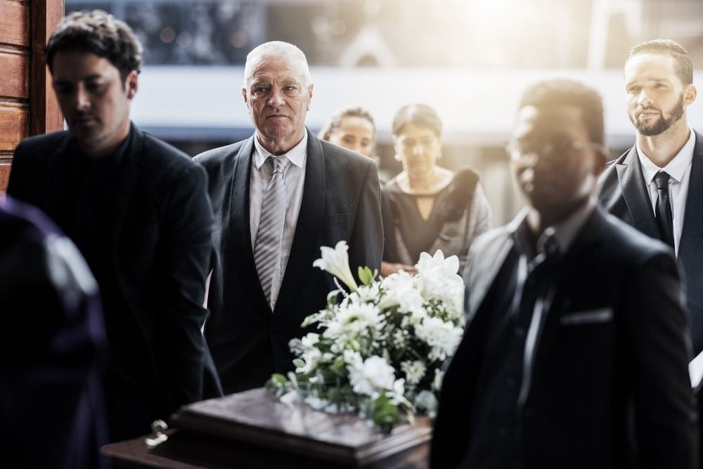 Mourners gather around a casket with white flowers during a funeral service