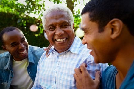 Three people smiling and laughing together outdoors in a sunny park
