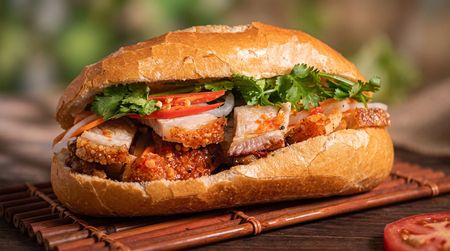 Hand holding a stuffed sandwich with lettuce, onions, and jalapeños on a warm orange background