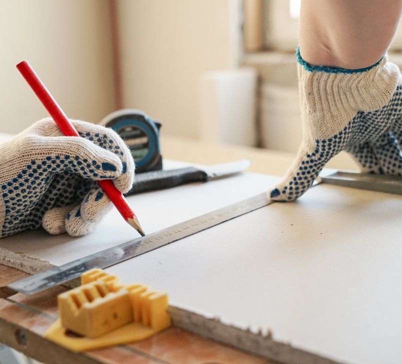 Hands wearing gloves measuring and marking a white surface with a pencil and ruler.