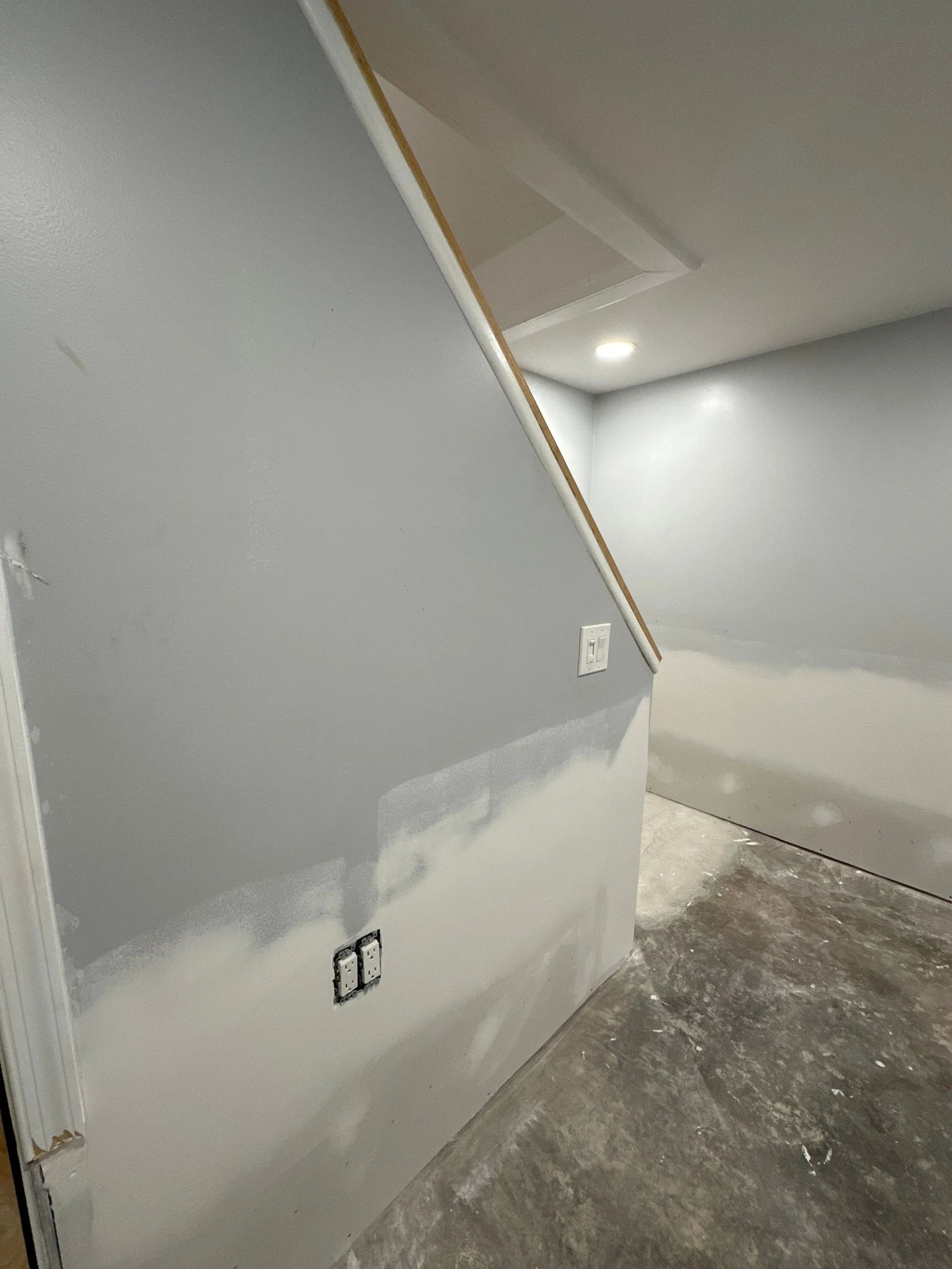 Interior room under renovation with gray walls, unfinished lower drywall, and exposed concrete floor