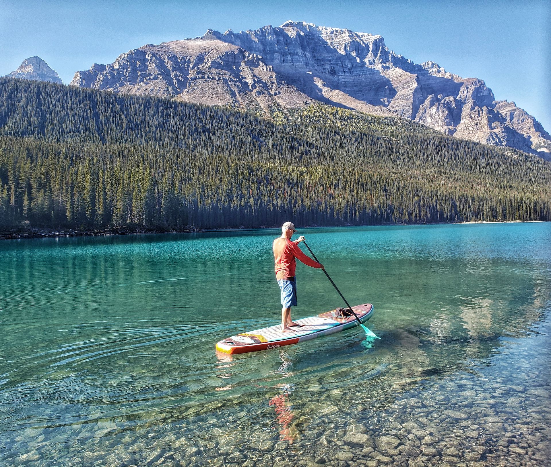 Person paddleboarding on a turquoise mountain lake with rocky peaks in the background