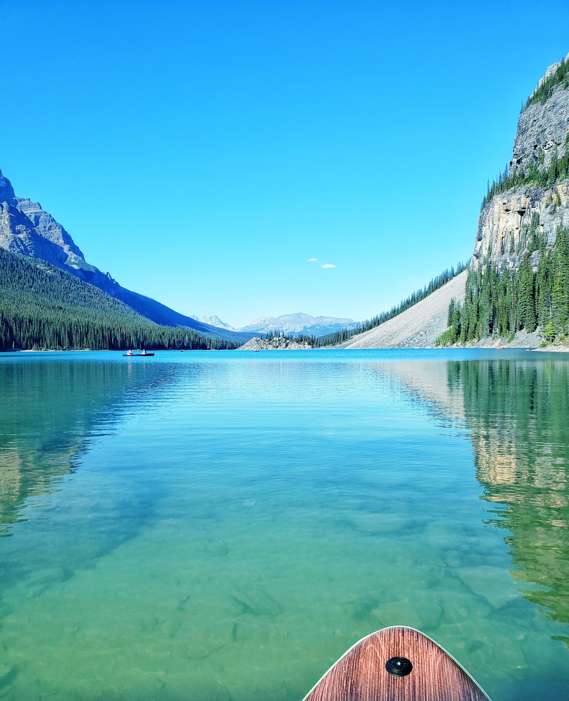 Crystal-clear lake with mountain cliffs and blue sky, viewed from a canoe at the bottom edge
