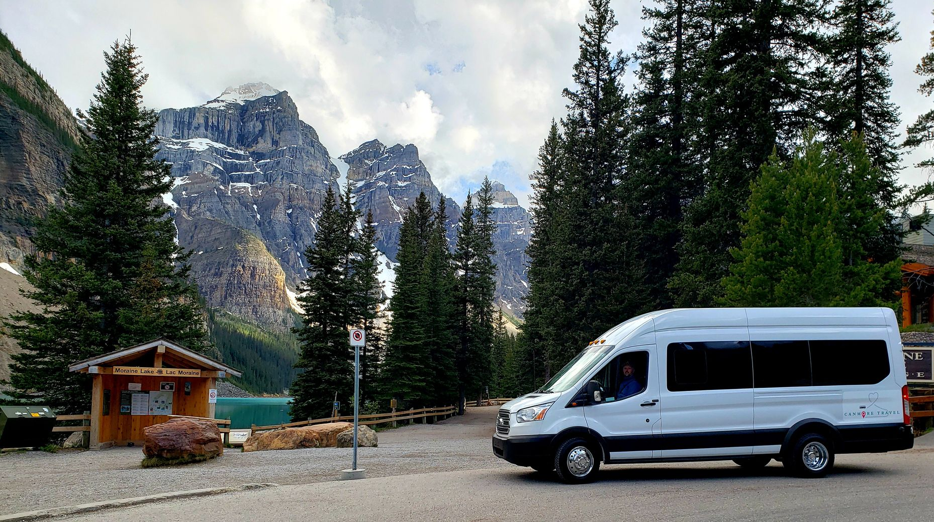 White van parked by a forest lake with mountains and evergreen trees in the background