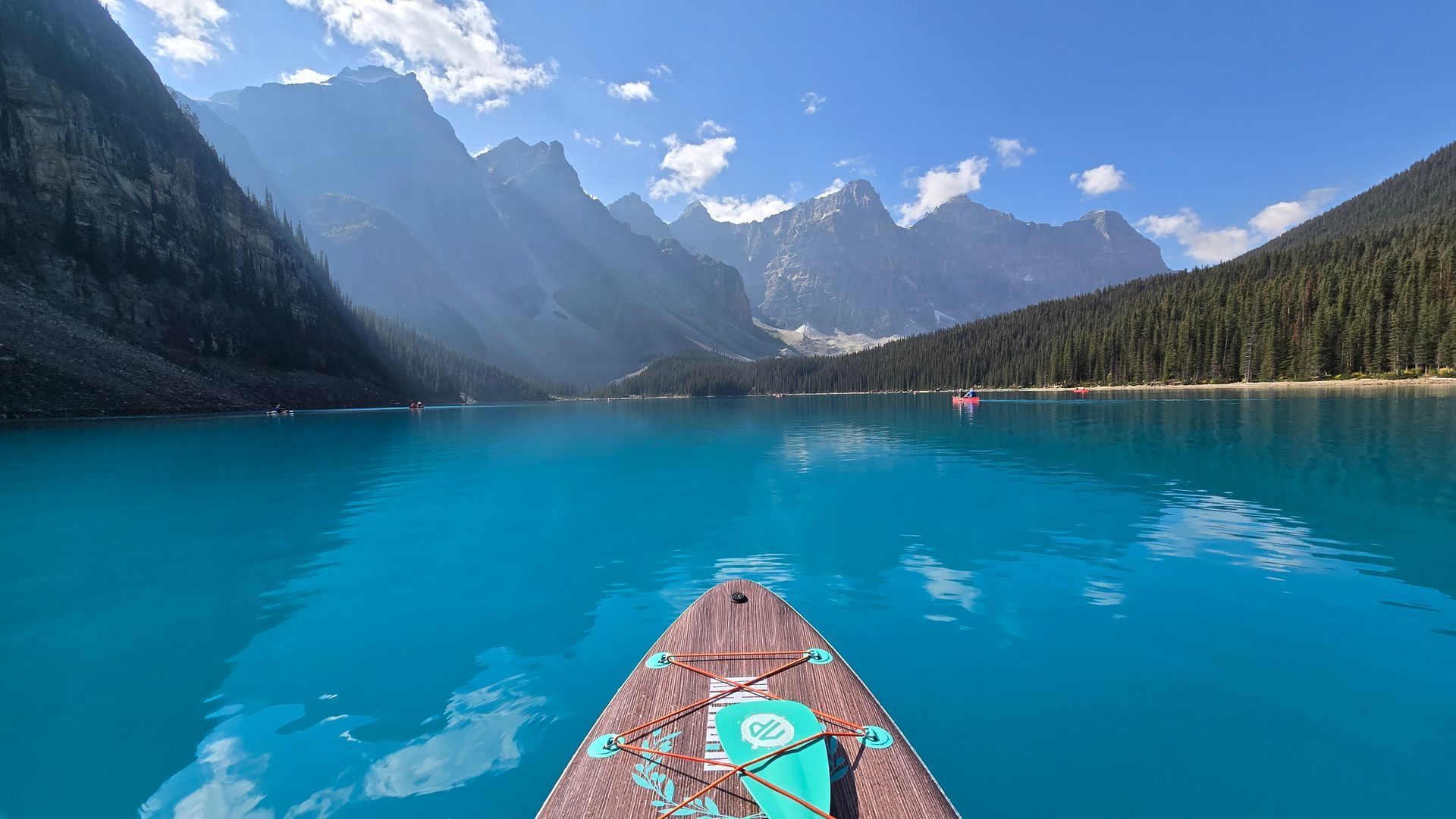 Paddling a canoe on a turquoise mountain lake with snow-capped peaks and forested shores