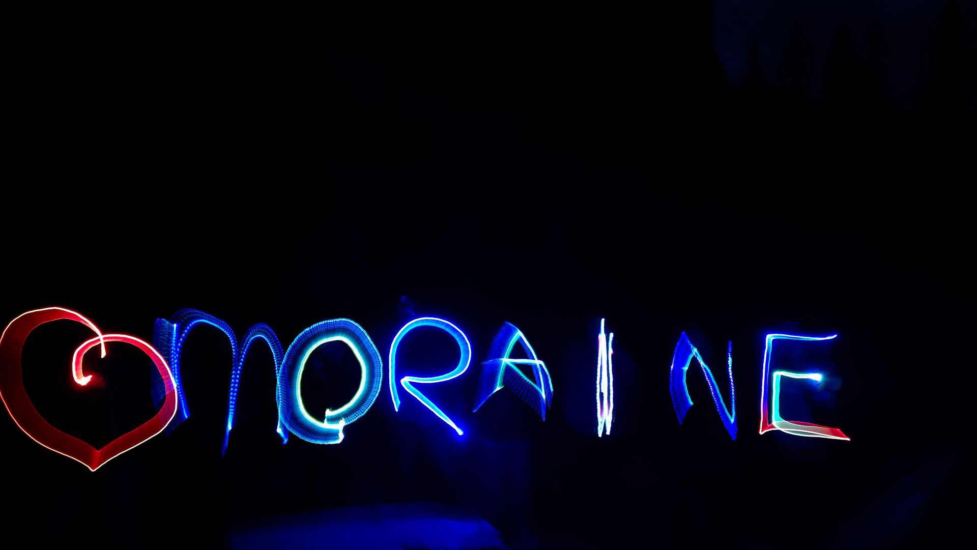 Glowing red and blue neon sign spelling “NORAINE” on a dark background