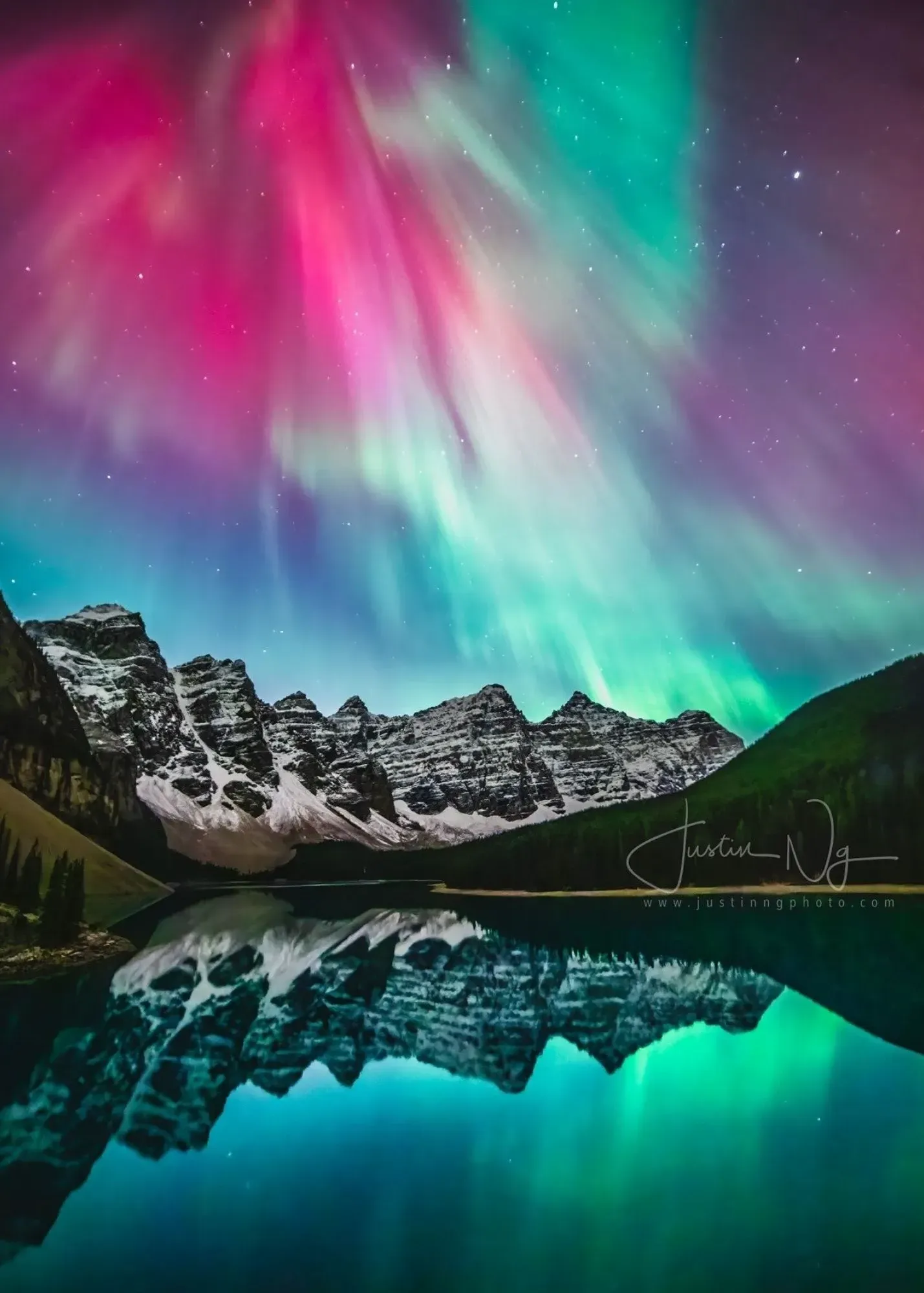 Aurora lights over snow-capped mountains reflected in Moraine Lake at dusk