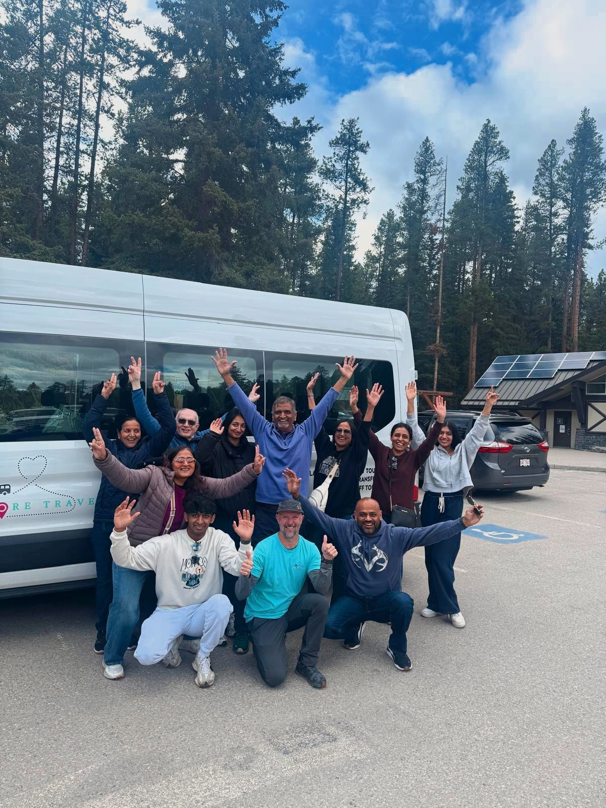 Group of people posing and cheering in front of a white van outdoors by tall trees