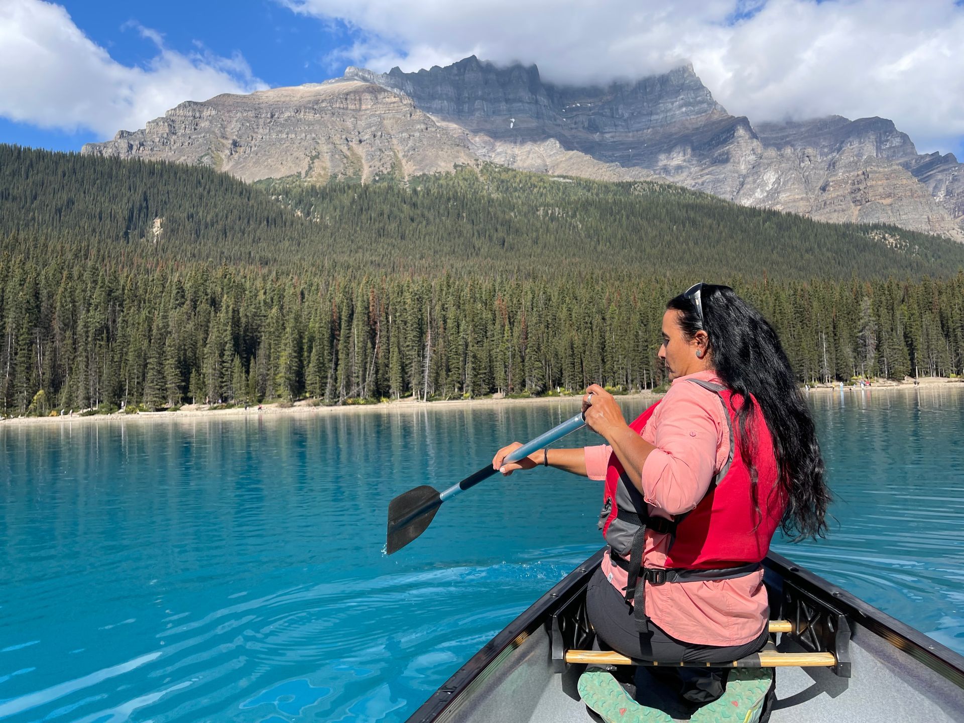 Person kayaking on a turquoise mountain lake with forest and rocky peaks in the background