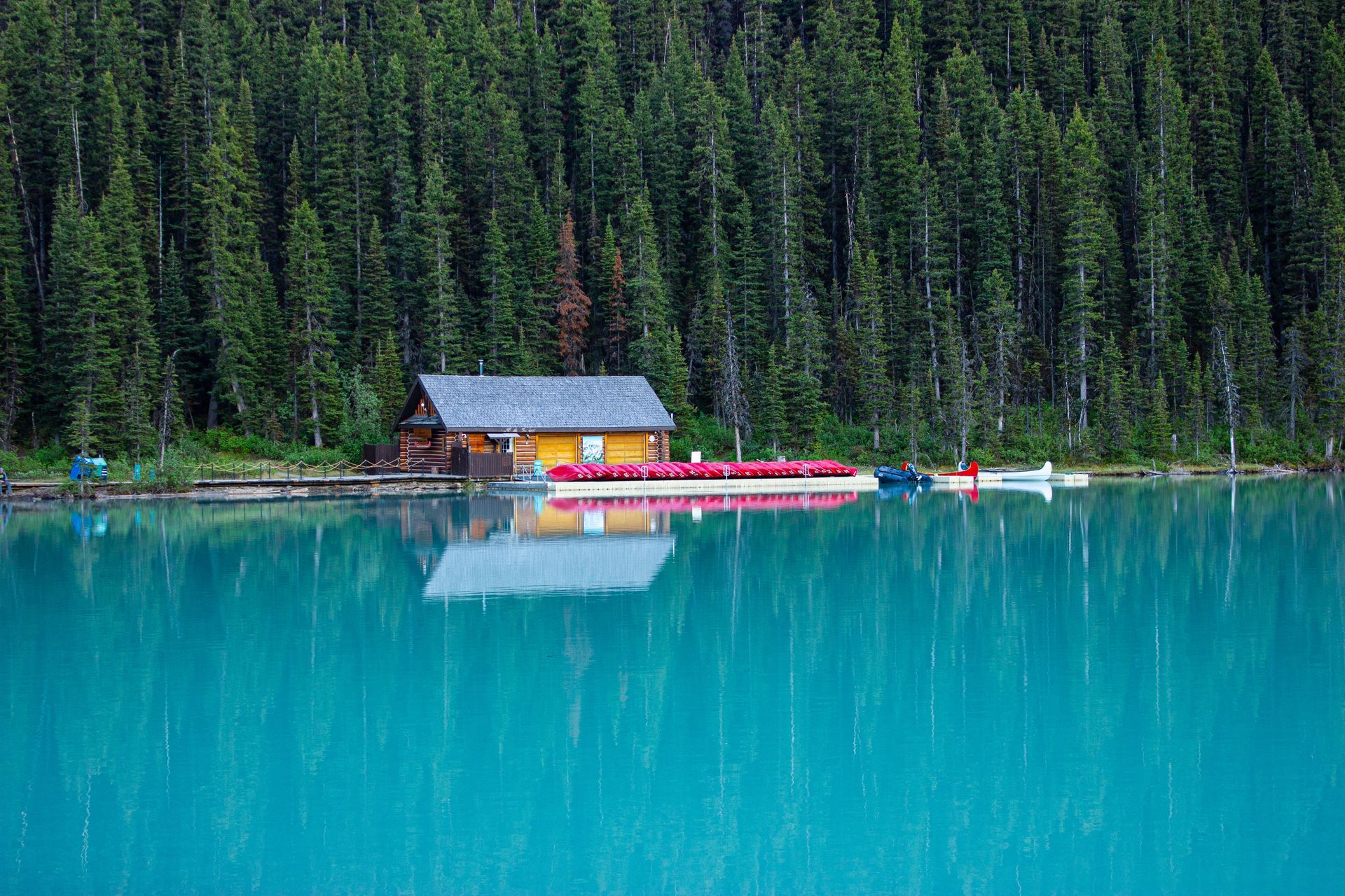 Red cabins and boats on a turquoise lake beside dense evergreen forest