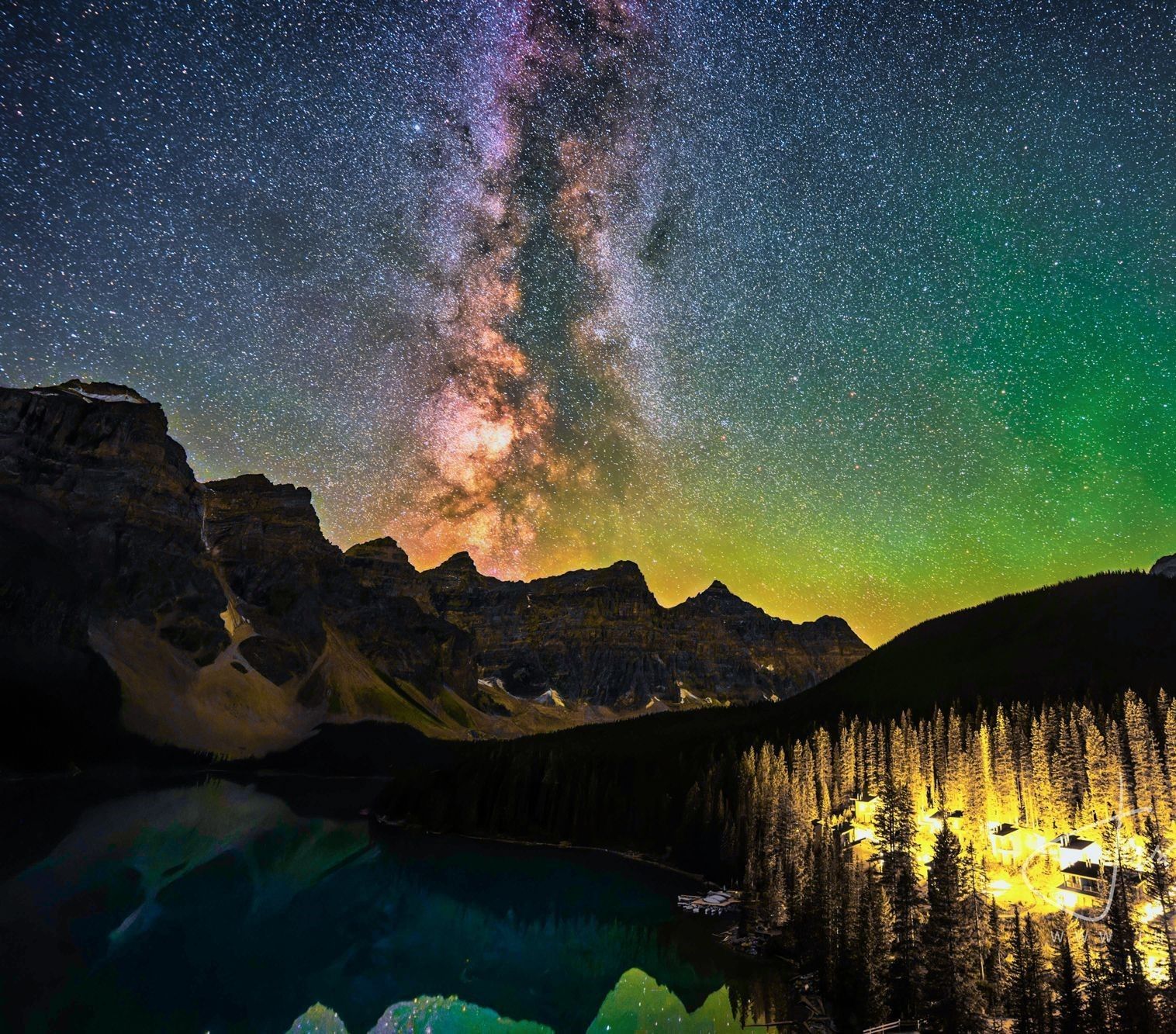 Starry Milky Way over mountains, lake, and glowing forest under a colorful night sky