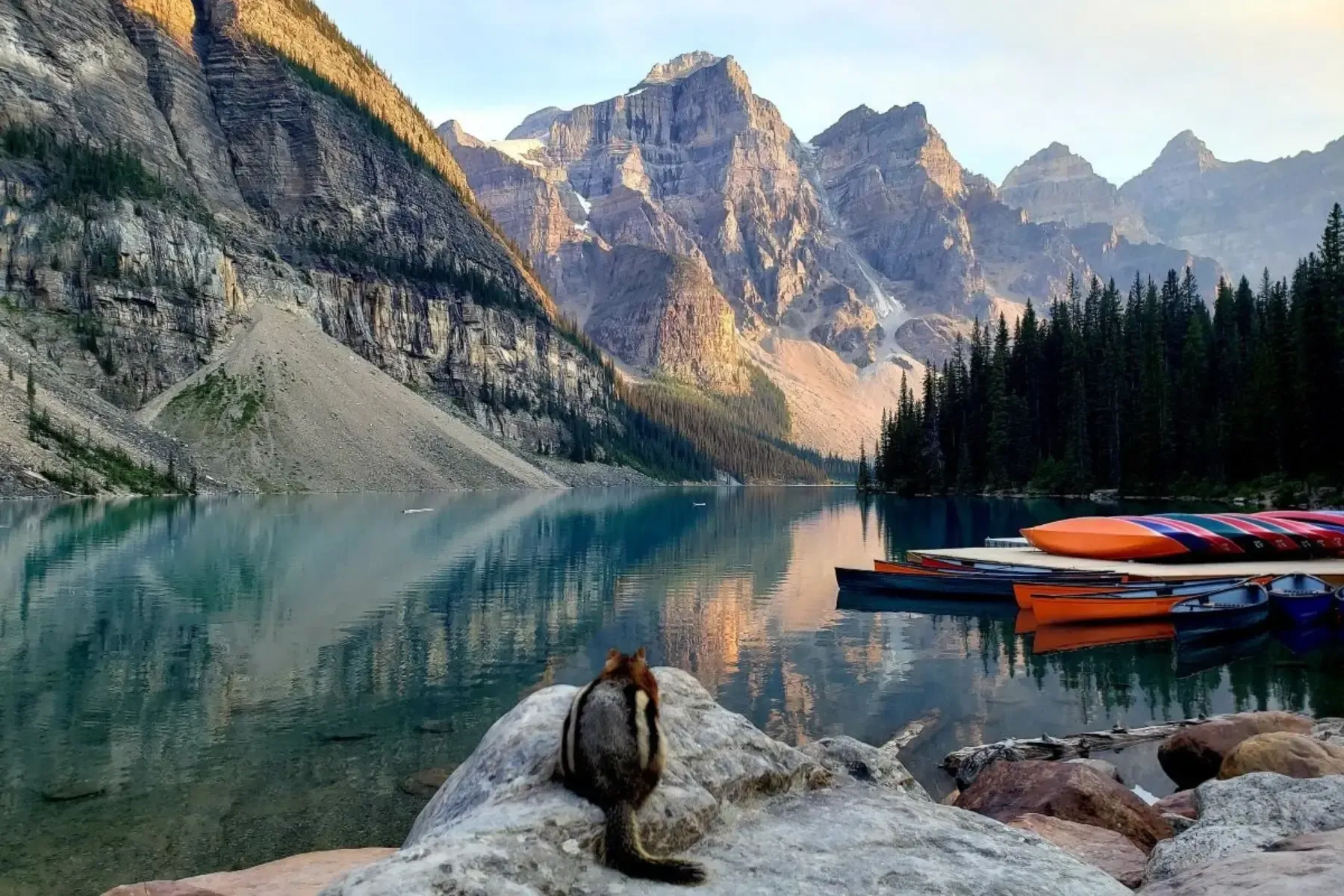 Moraine Lake with a squirrel on a rock, canoes on the shore, and tall peaks reflected in calm water