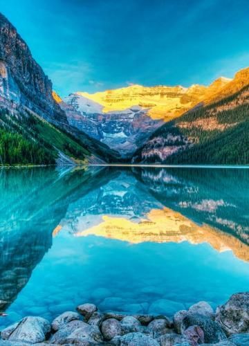Snow-capped mountains and a turquoise lake reflecting the peaks, with rocks in the foreground