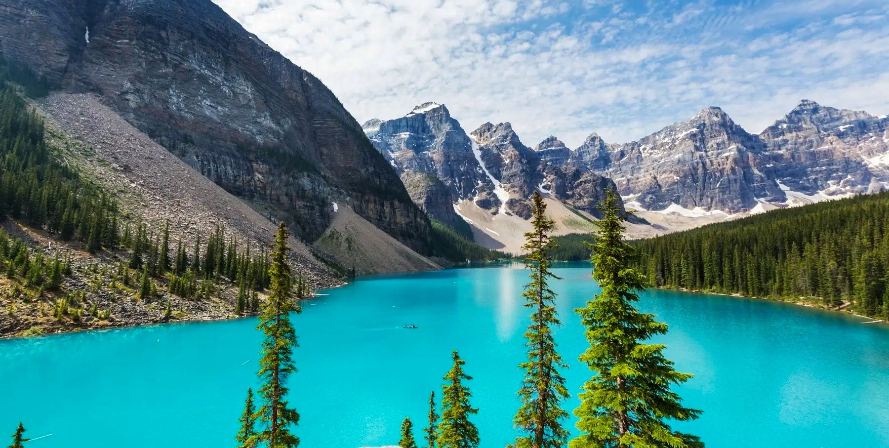 Turquoise alpine lake with pine trees and jagged mountains under a clear sky