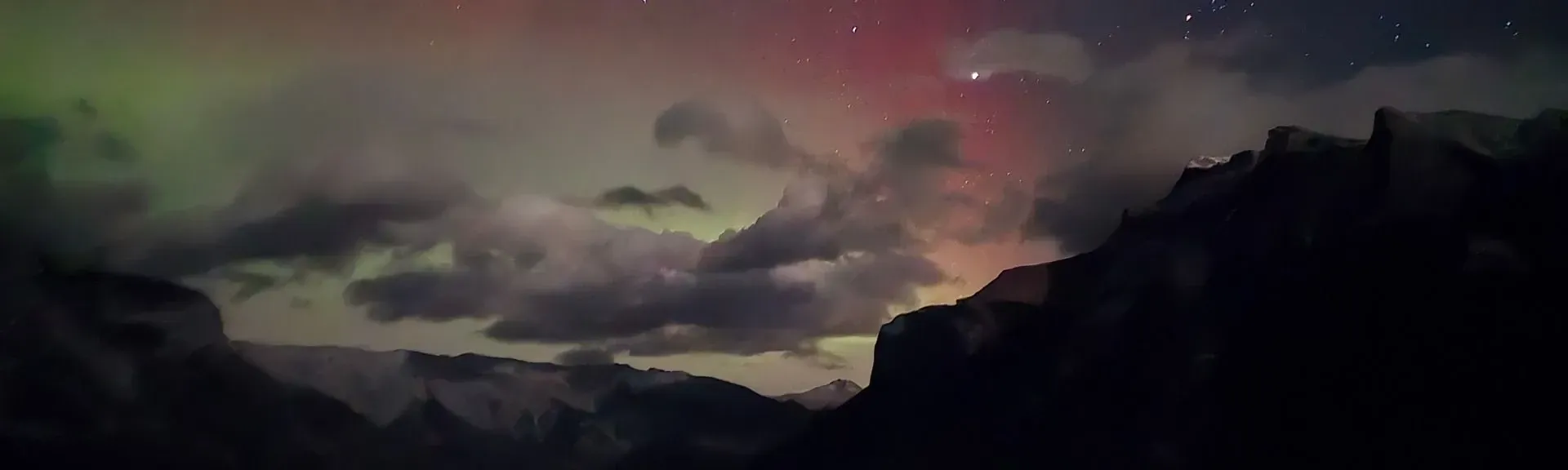 Dramatic sunset sky with purple clouds over dark mountain silhouettes and a glowing horizon