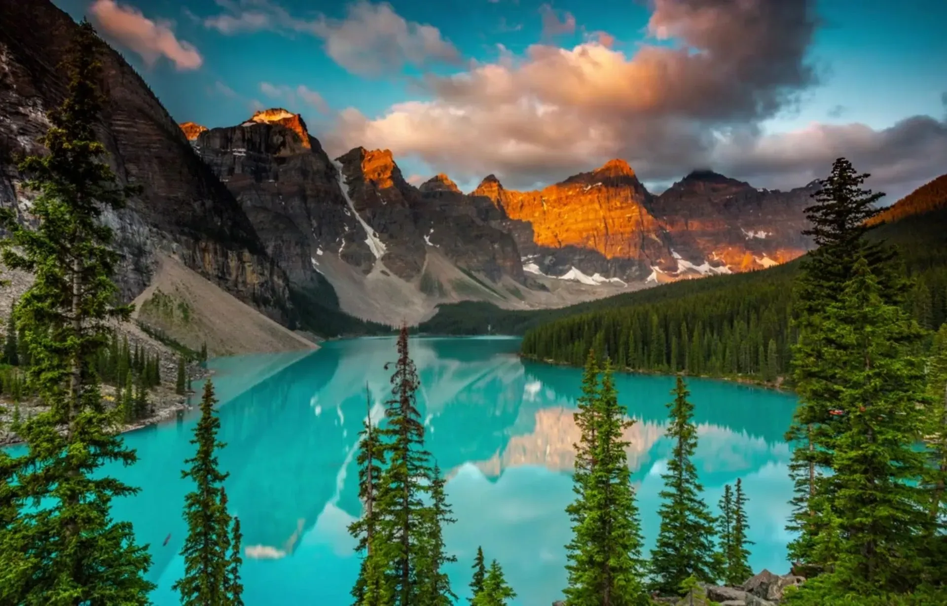 Moraine Lake with pine trees, rocky peaks, and glowing sunset clouds