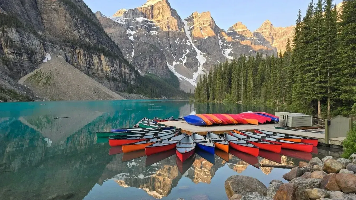 Colorful canoes on Moraine Lake with pine trees and rocky peaks reflected in the water