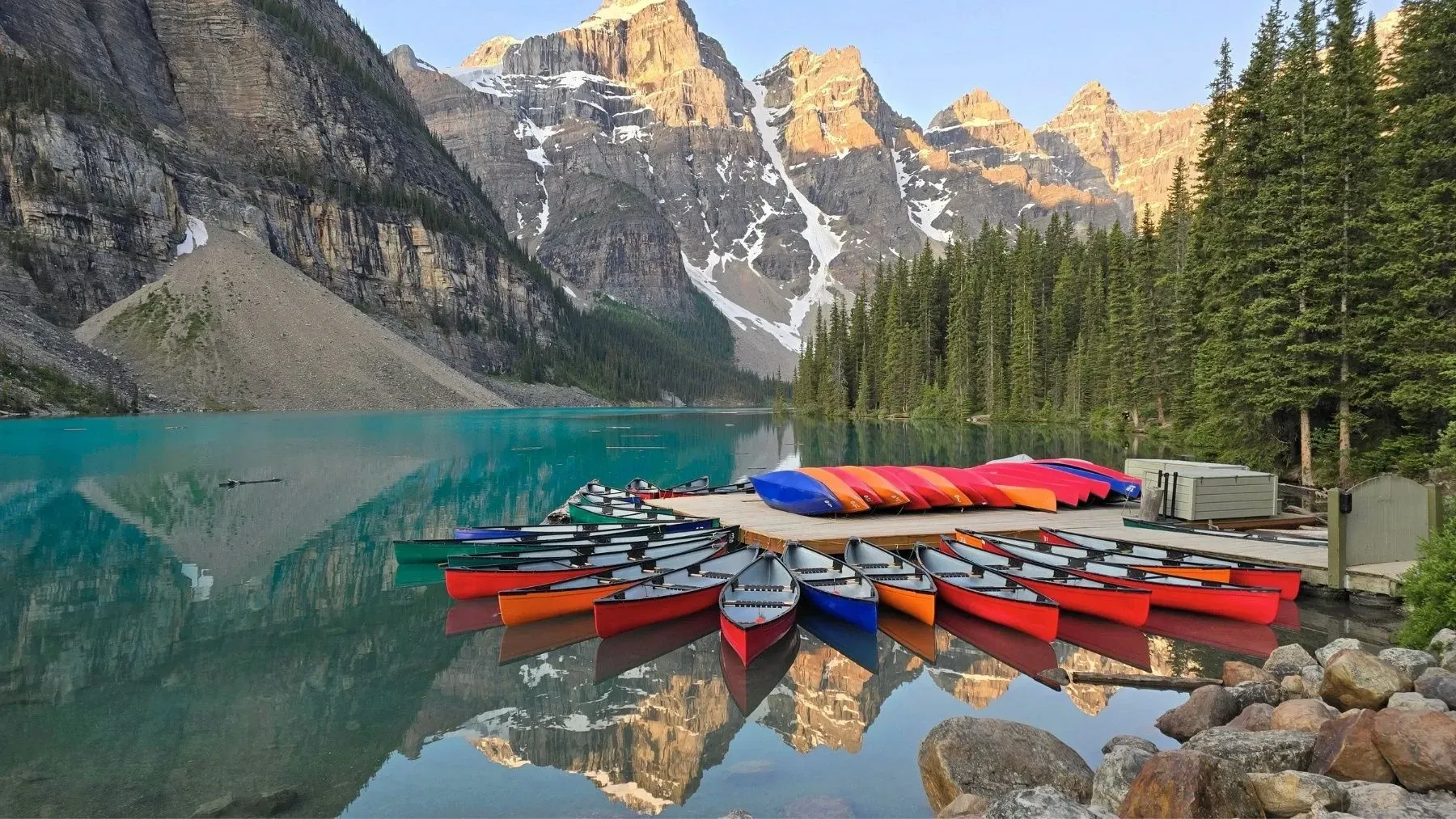 Colorful canoes on Moraine Lake with pine trees and rocky peaks reflected in the water