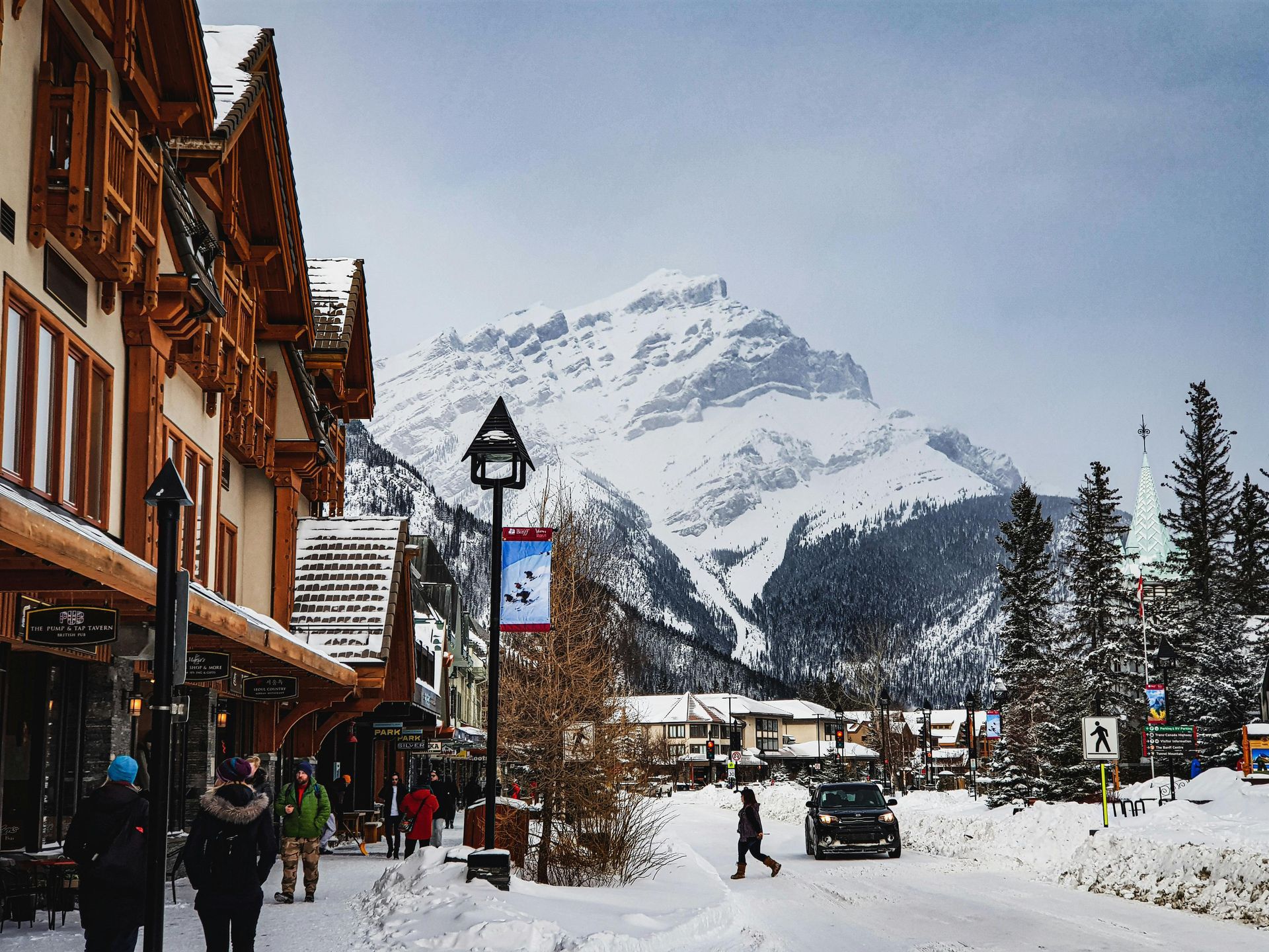 Snowy mountain village street with wooden shops, pedestrians, and a ski slope in the background