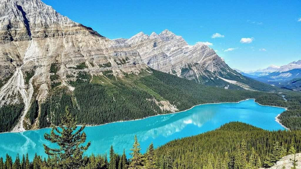 Turquoise mountain lake with pine forest and rugged snow-capped peaks under a clear blue sky