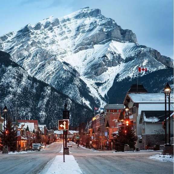 Snowy mountain over a small town street with Canadian flags at dusk