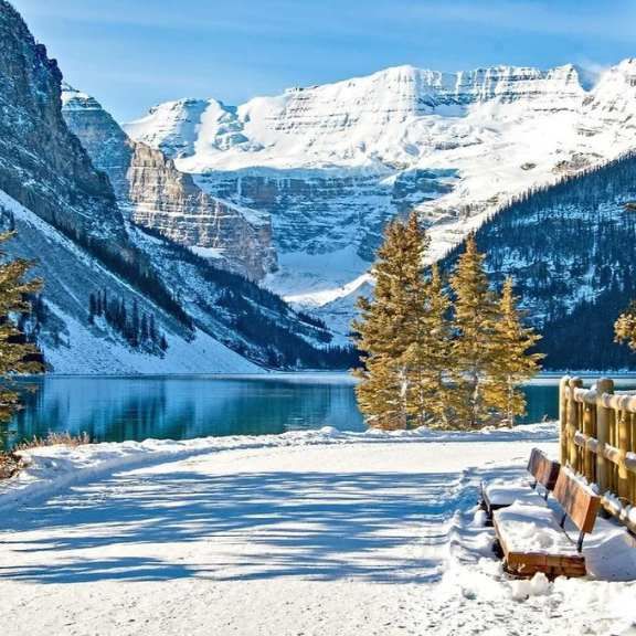 Snowy mountain lake with blue water, snowy peaks, and pine trees under a bright winter sky