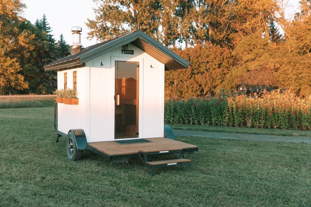 A small white house on wheels is sitting in the middle of a grassy field.