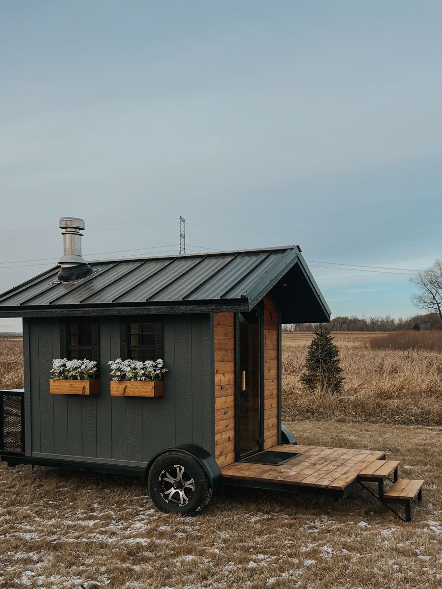 A small house on wheels is parked in a field.