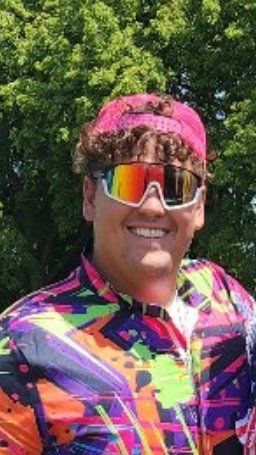 A man wearing sunglasses and a pink headband is smiling.