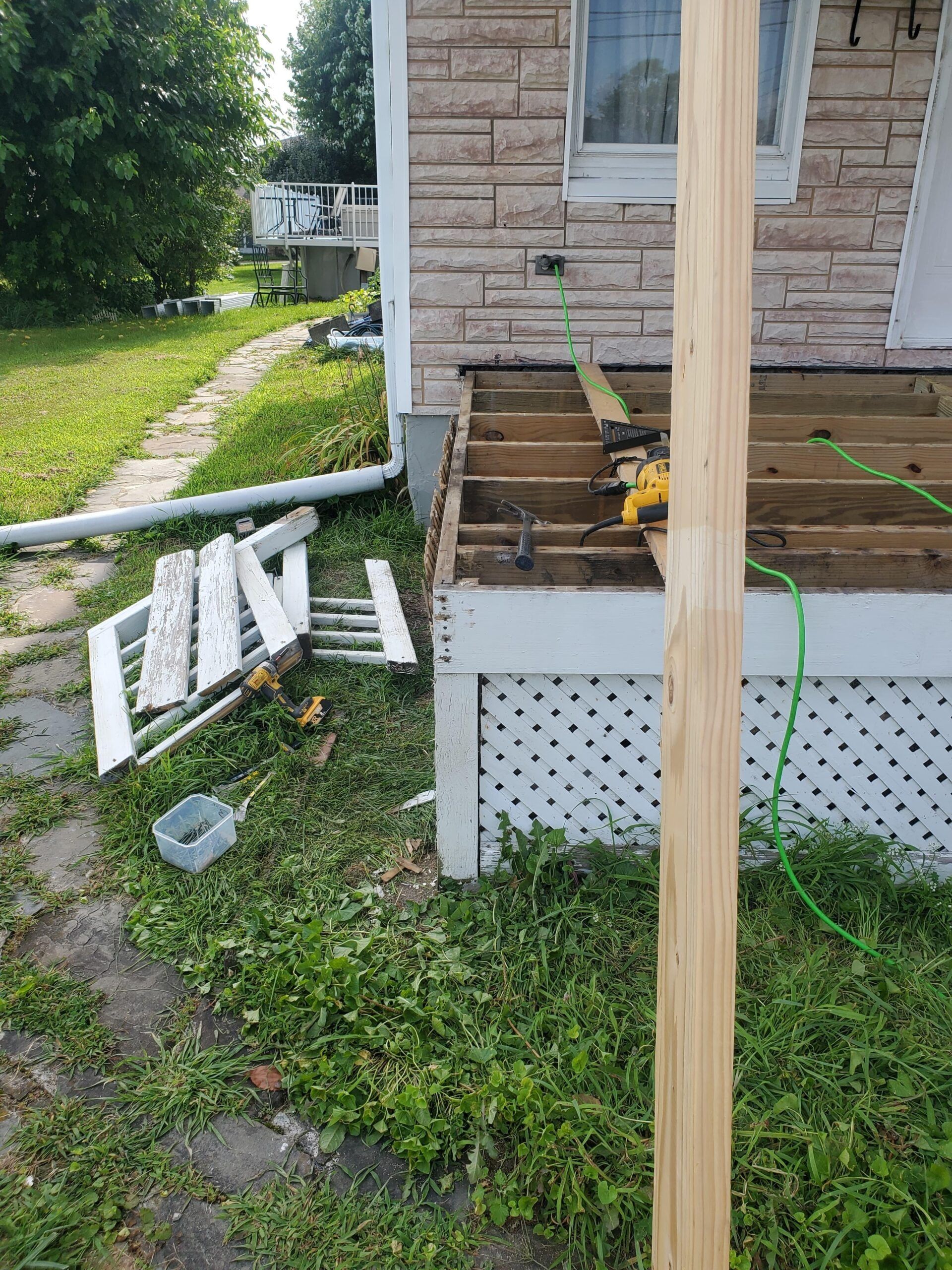 Porch deck under construction, tools and materials scattered.  Building is light stone and white lattice.