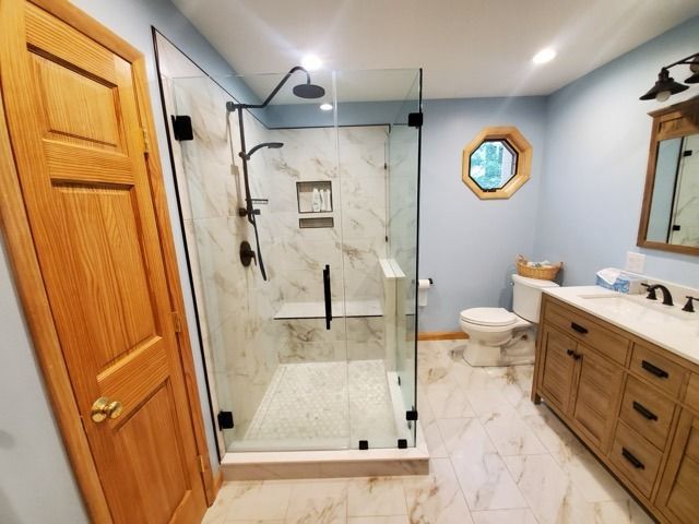 Bathroom with walk-in shower, light blue walls, wood vanity and door, octagonal window, white marble tile.