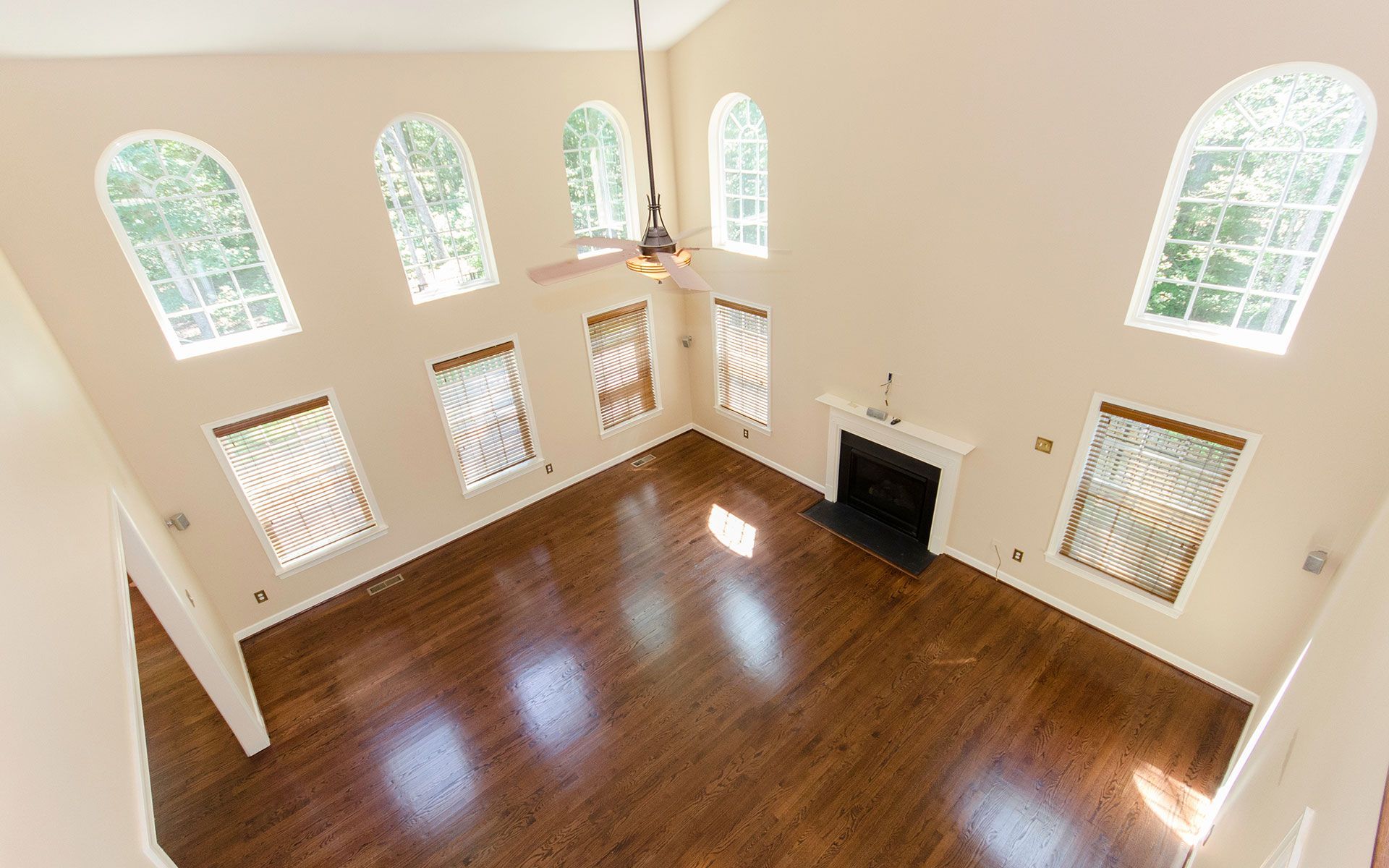 High-angle view of a large room with hardwood floors, fireplace, and arched windows.