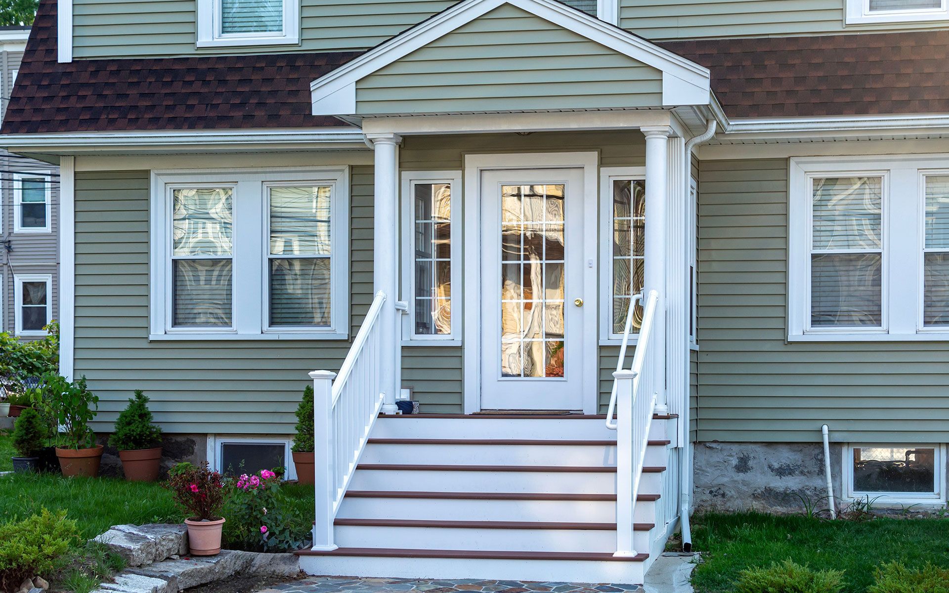 Green house with white trim, front porch with steps and door.