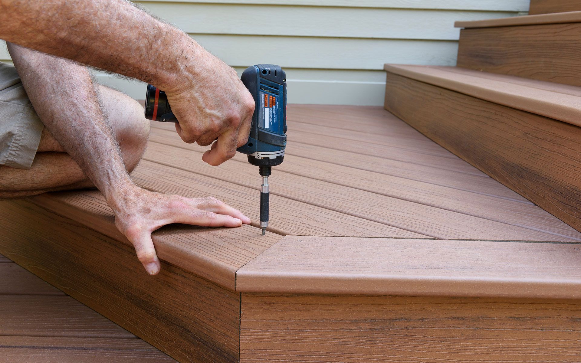 Person using a power drill to install deck boards on outdoor steps.