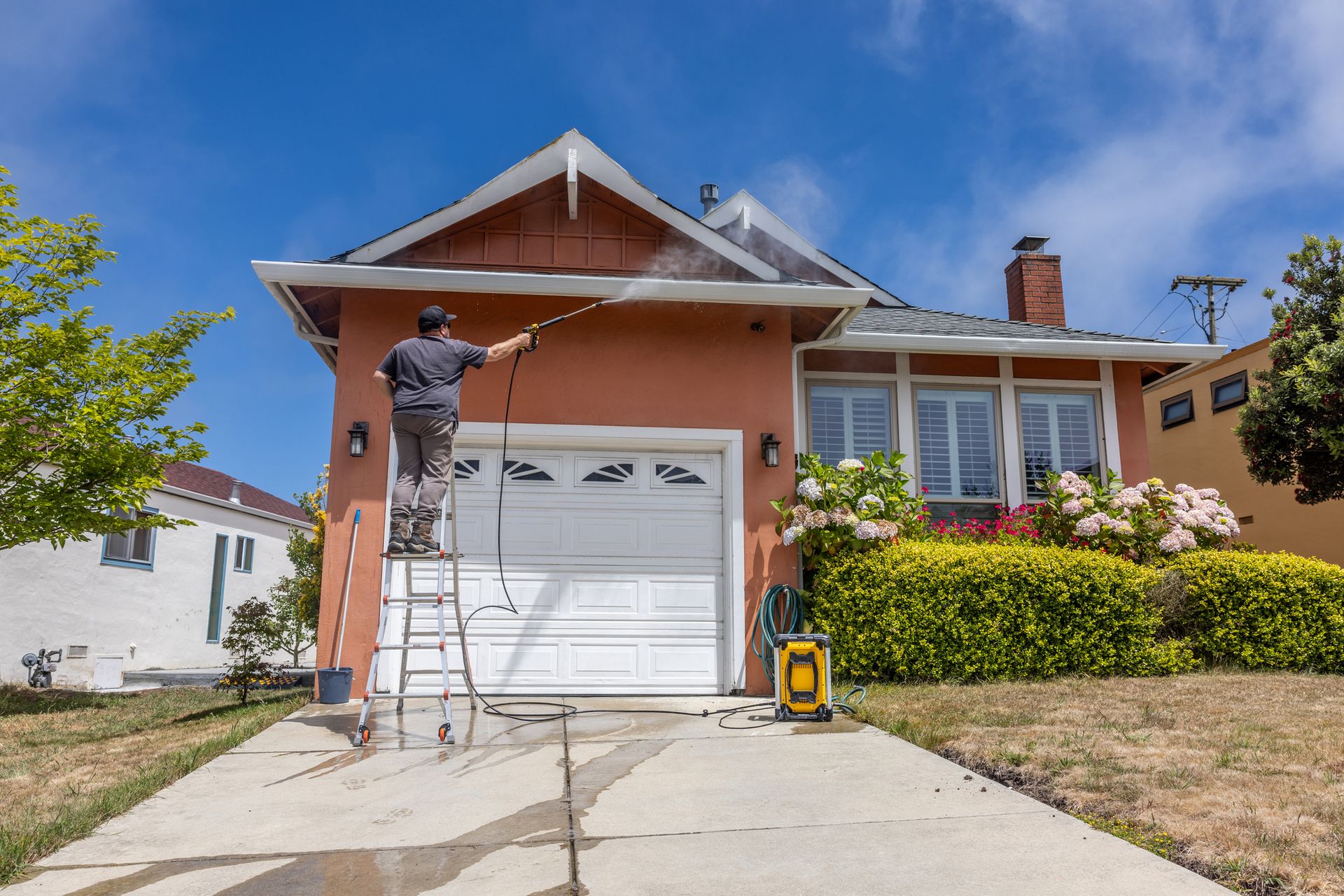 A man is standing on a ladder washing the side of a house.